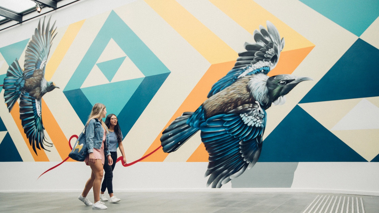 Two girls walking by a tui mural on a wall