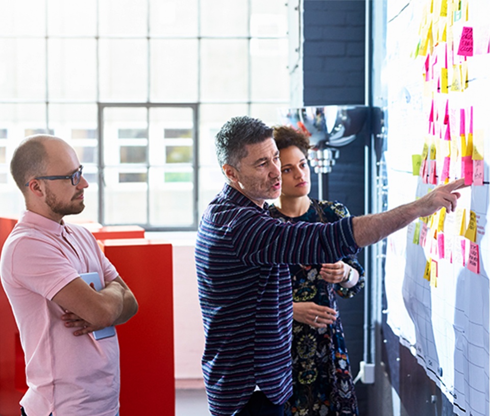 Group of three colleagues discussing work on a white board 