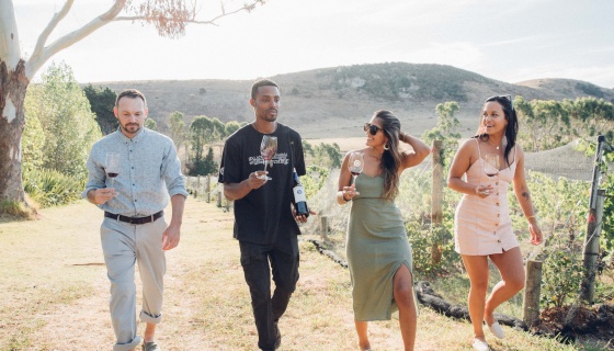 A group of friends holding glasses of wine and walking through a vineyard on Waiheke Island Auckland