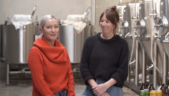 Two women standing front of large kombucha brewing vats