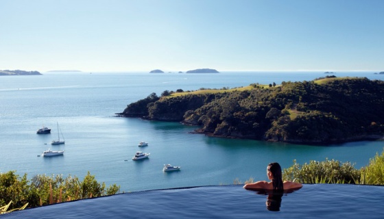 A woman at the edge of an infinity pool looking out to ocean and island views on Waiheke Island