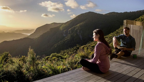 Couple looking at sunset from deck with forest and hills (credit: ATEED / Todd Eyre)